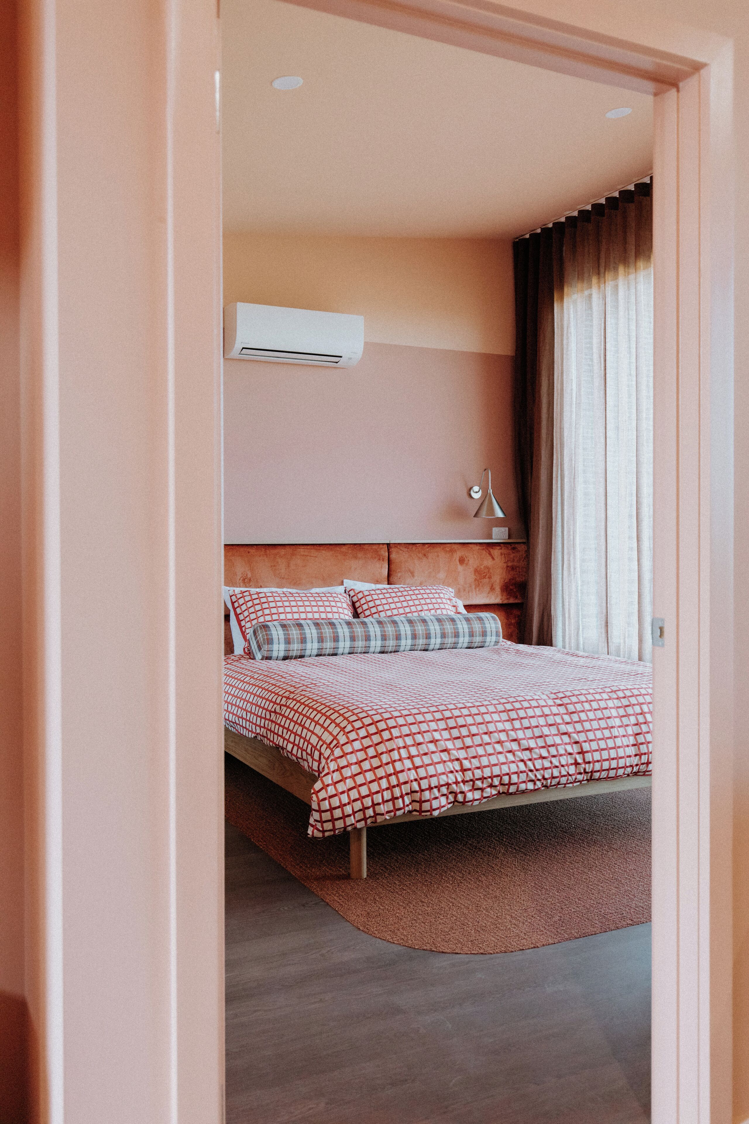 A bedroom with a bed, a headboard, a bedside table, a lamp, and a window with curtains.