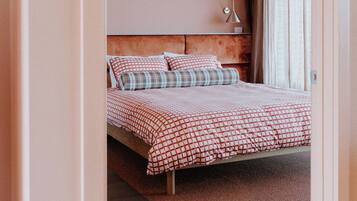 A bedroom with a bed, a headboard, a bedside table, a lamp, and a window with curtains.