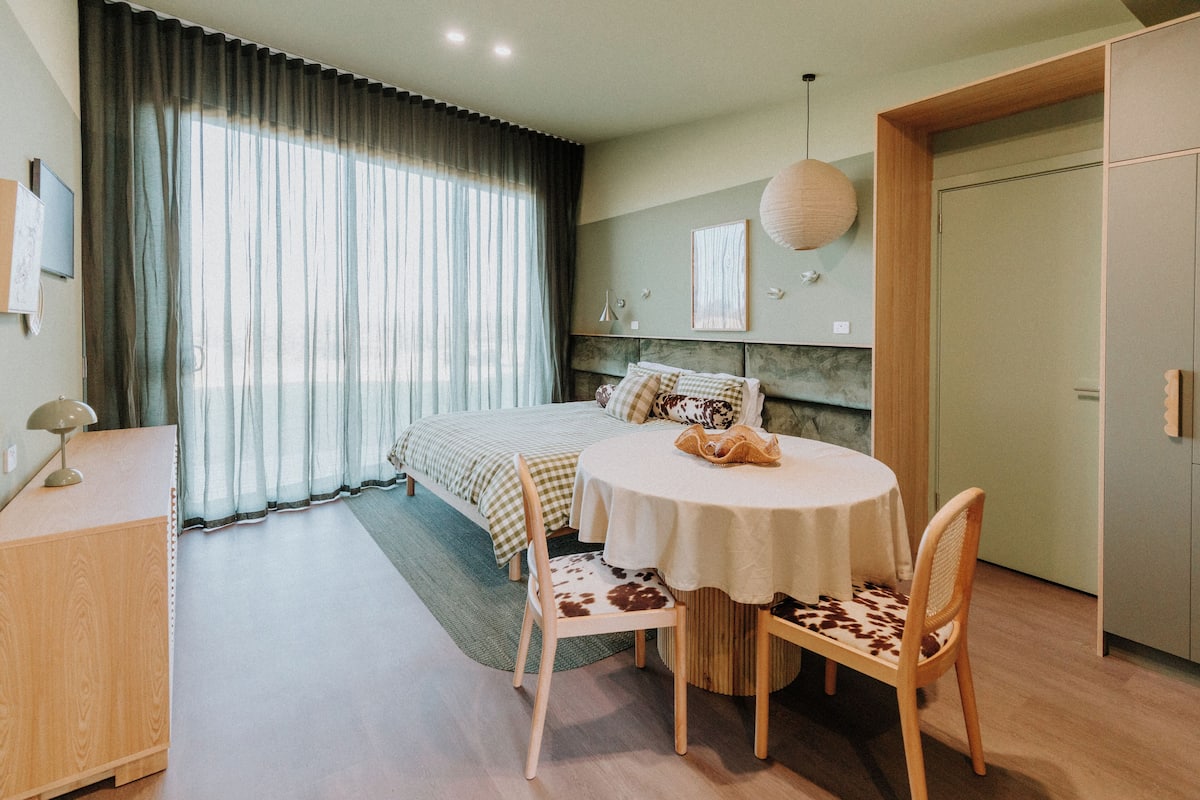 A modern bedroom with a bed, a round table with two chairs, a desk, and a wardrobe.