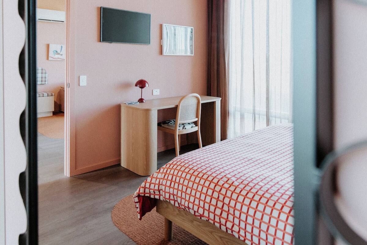 A bedroom with a bed, desk, chair, and a television on the wall.