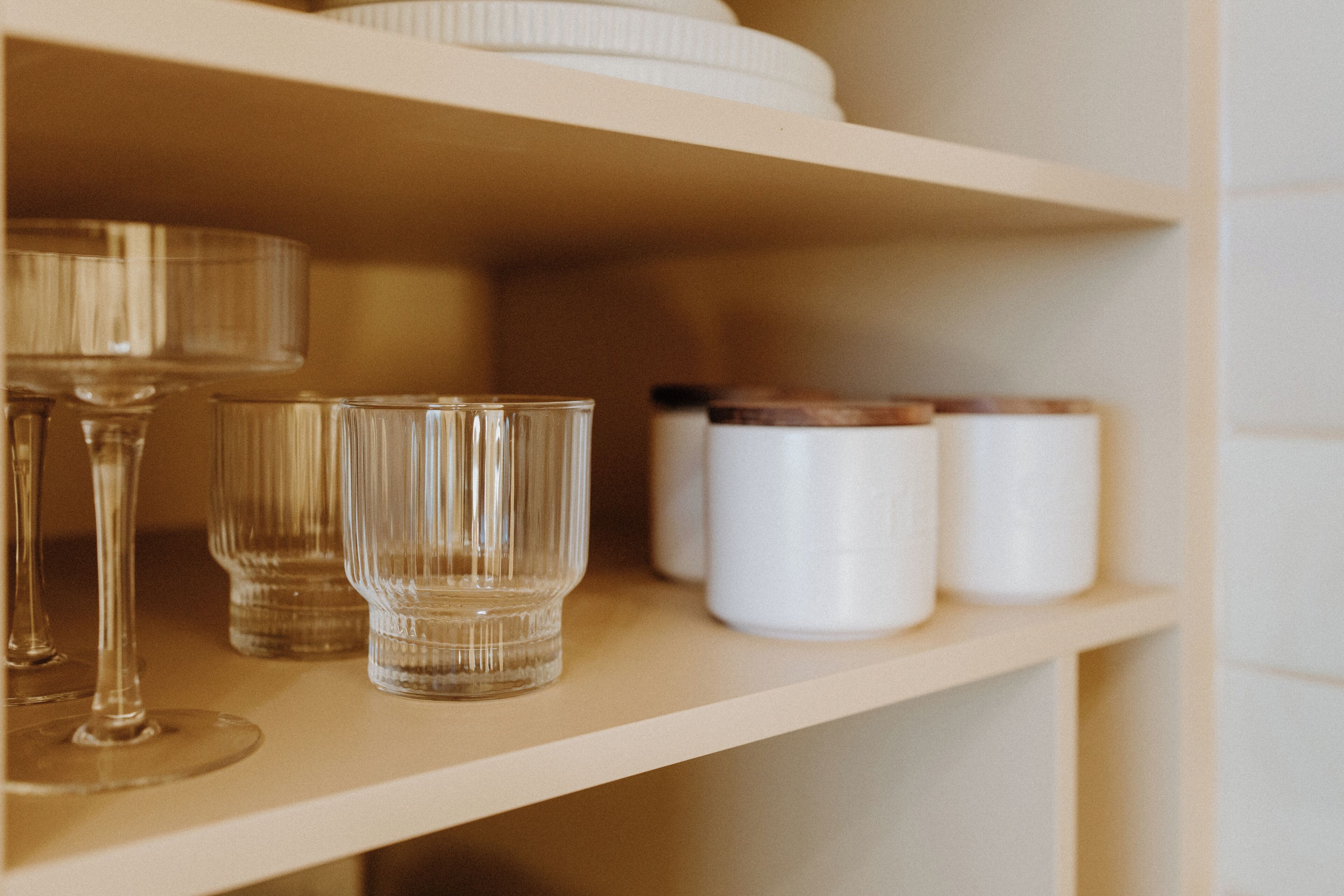 A shelf with clear glassware and white containers.
