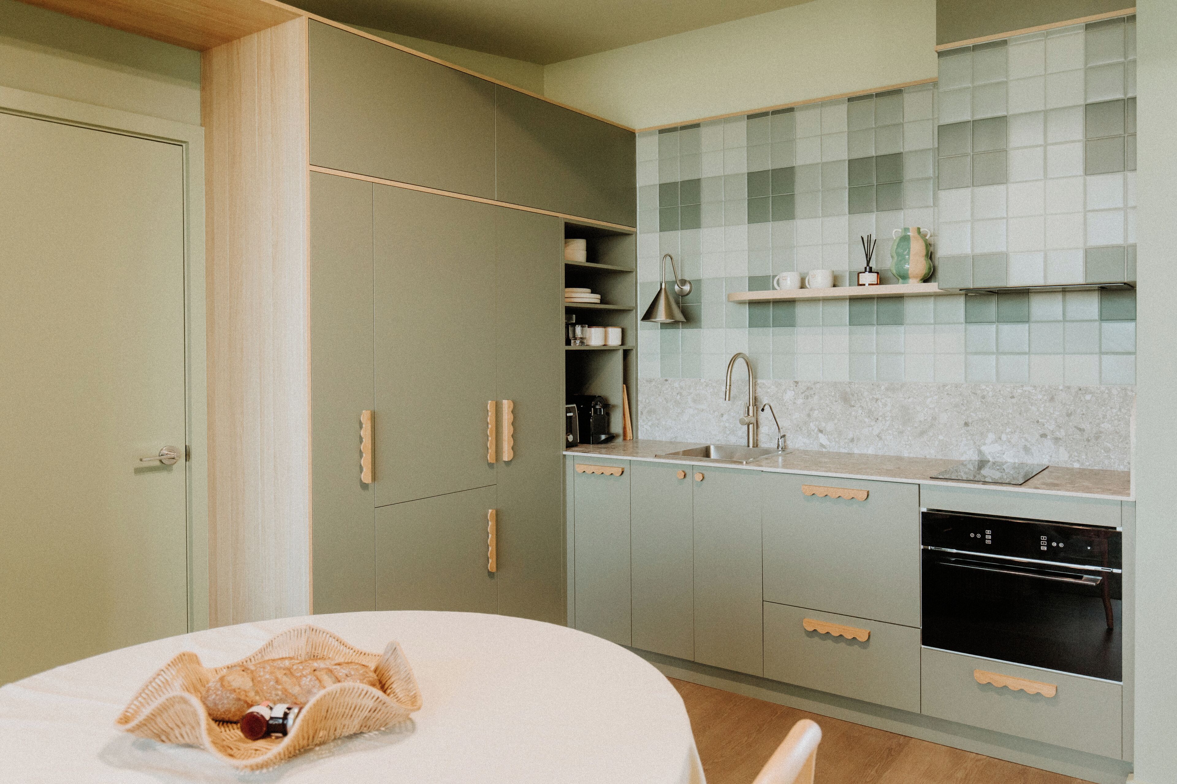 A modern kitchen with light green cabinets, a white countertop, and a built-in oven.
