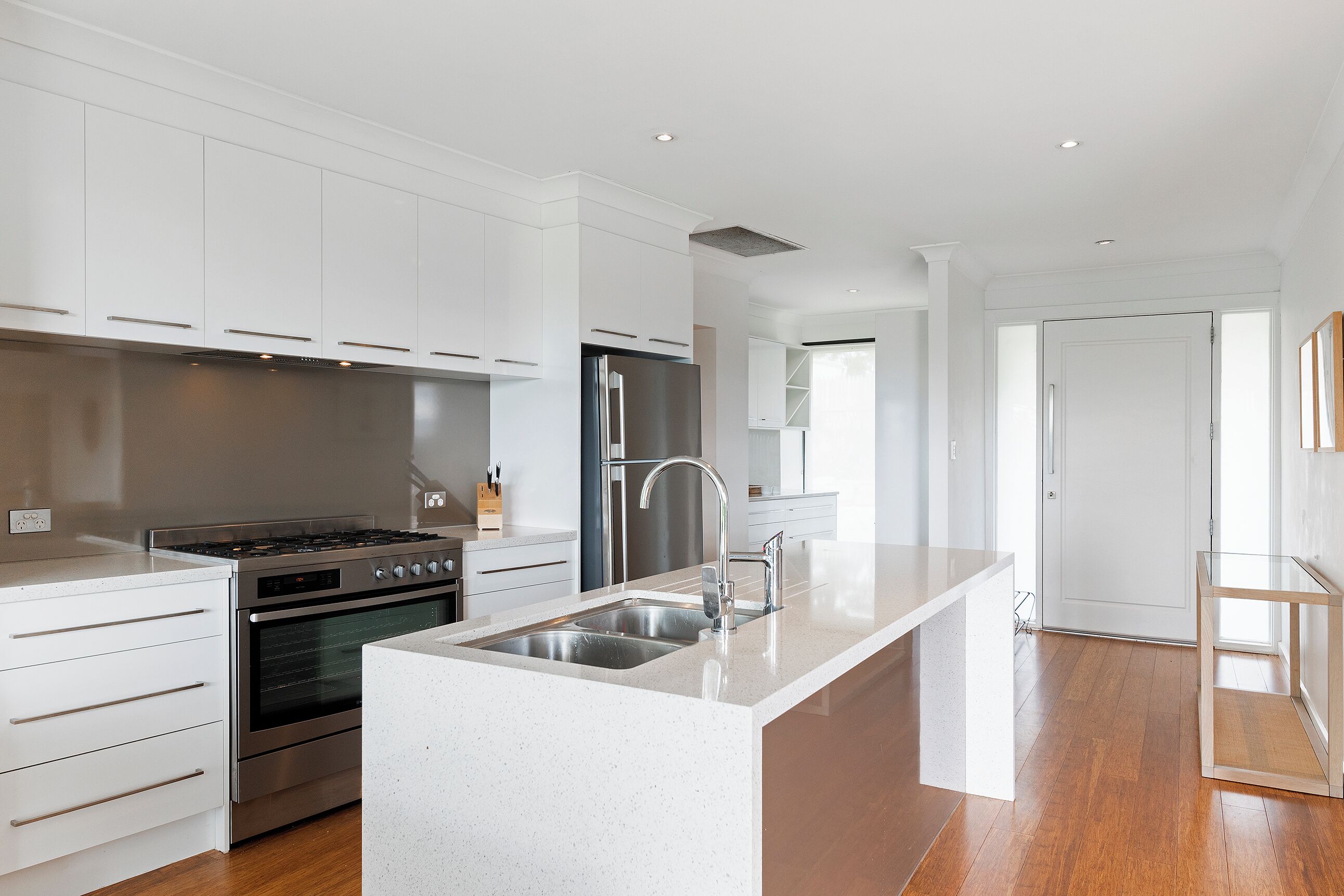 A modern kitchen with white cabinetry, stainless steel appliances, and a large island with a sink.