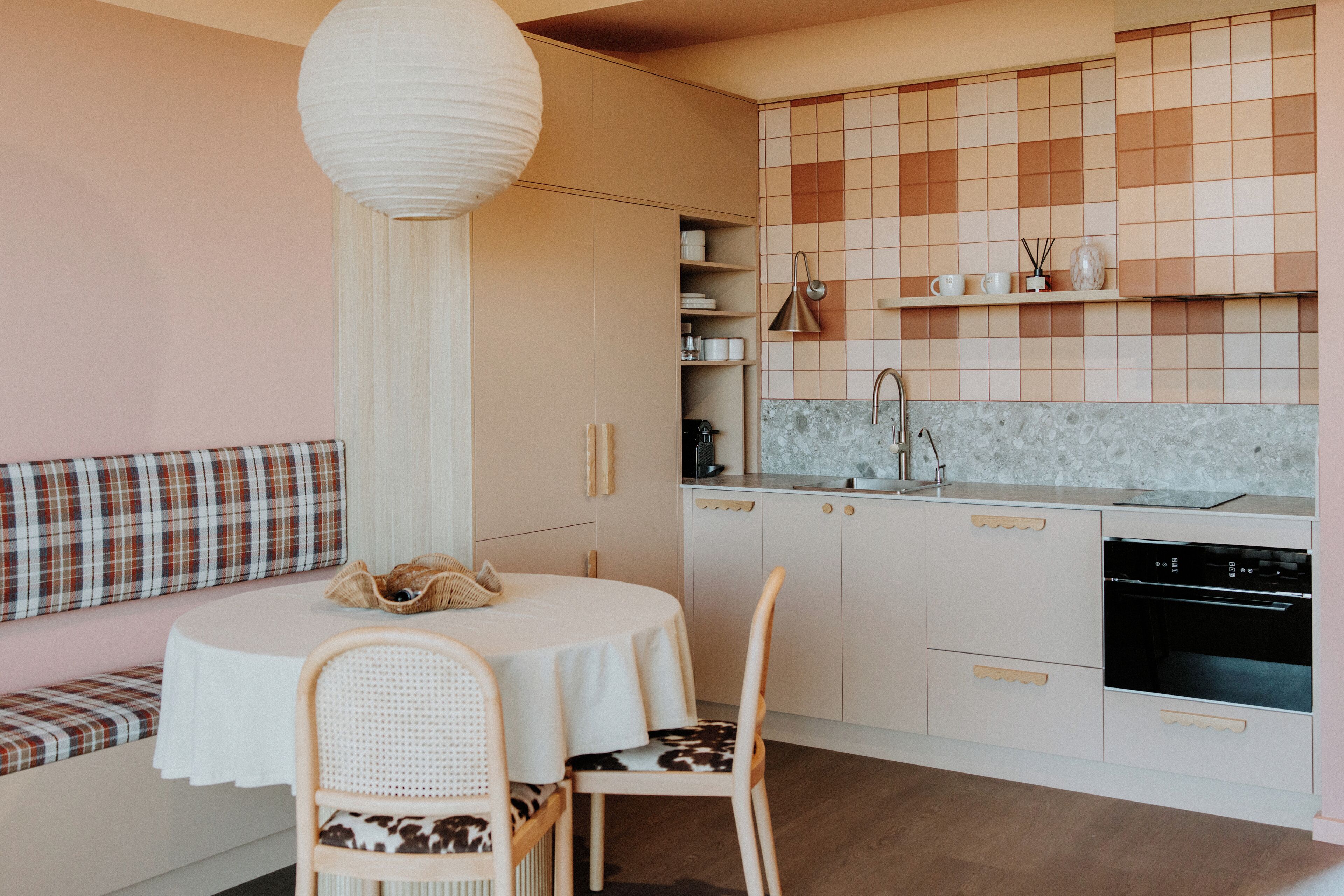 Una cocina moderna con una mesa de comedor redonda, dos sillas, un banco con cojín a cuadros y una lámpara colgante.