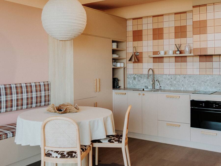 Una cocina moderna con una mesa de comedor redonda, dos sillas, un banco con cojín a cuadros y una lámpara colgante.