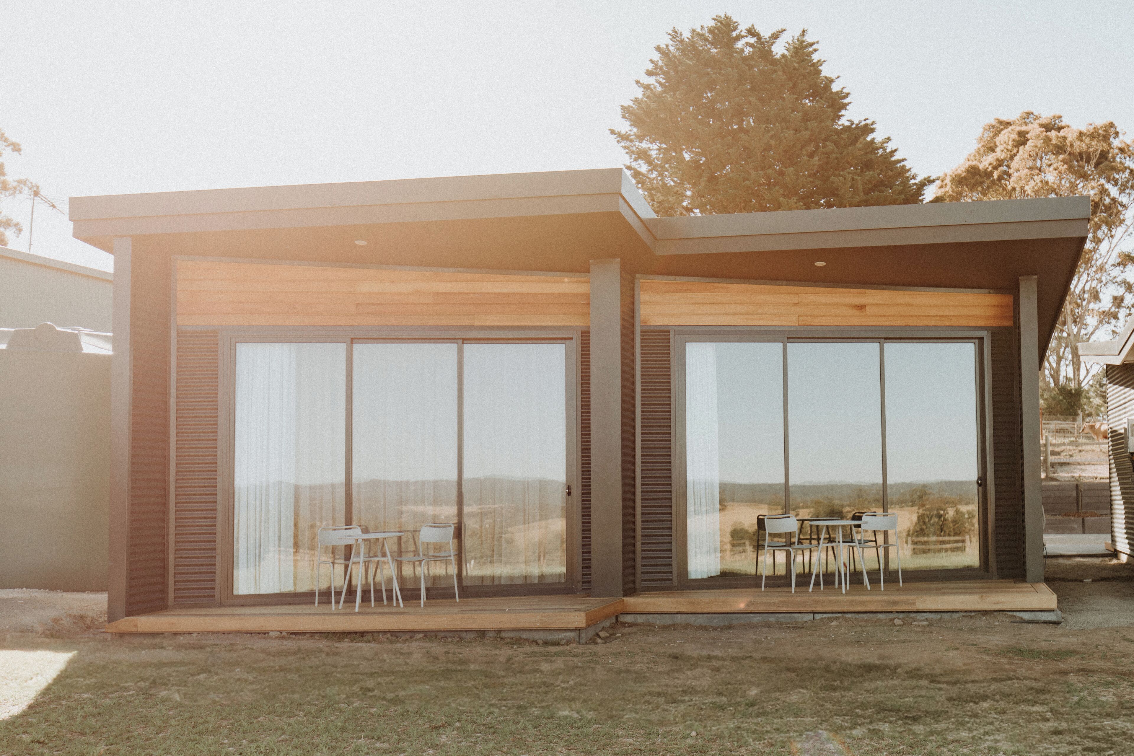 Une maison moderne dotée de grandes portes vitrées, d’un patio avec une table et des chaises, et offrant une vue sur le paysage environnant.