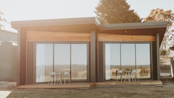 Une maison moderne dotée de grandes portes vitrées, d’un patio avec une table et des chaises, et offrant une vue sur le paysage environnant.
