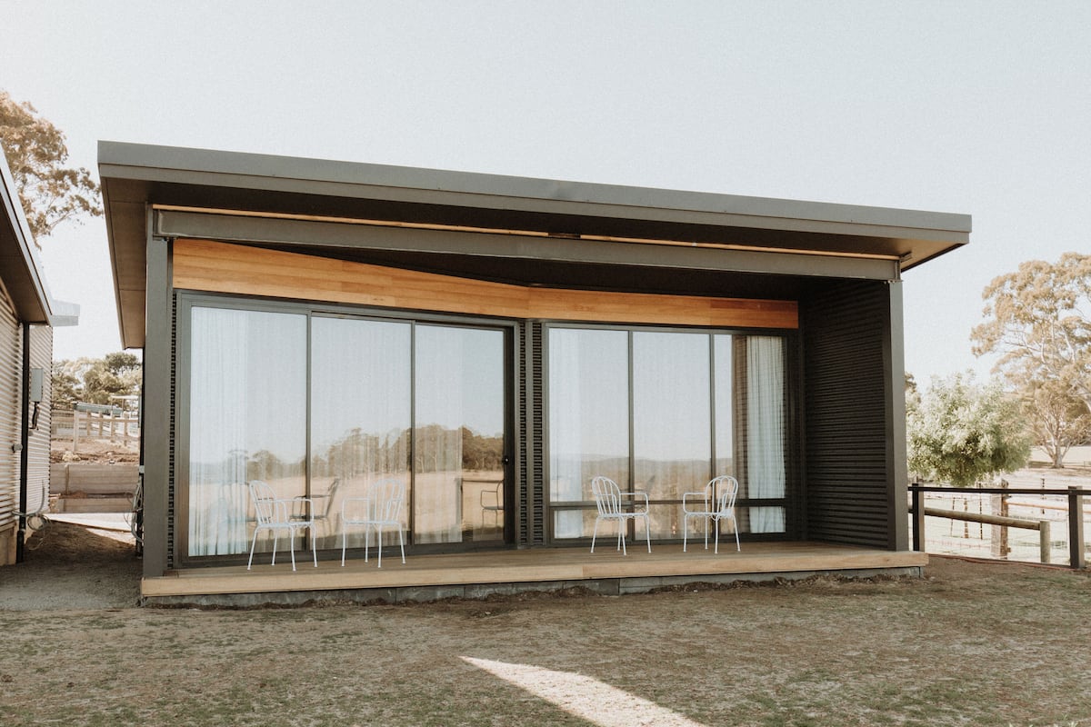 A modern building with large sliding glass doors, a wooden deck, and white chairs.