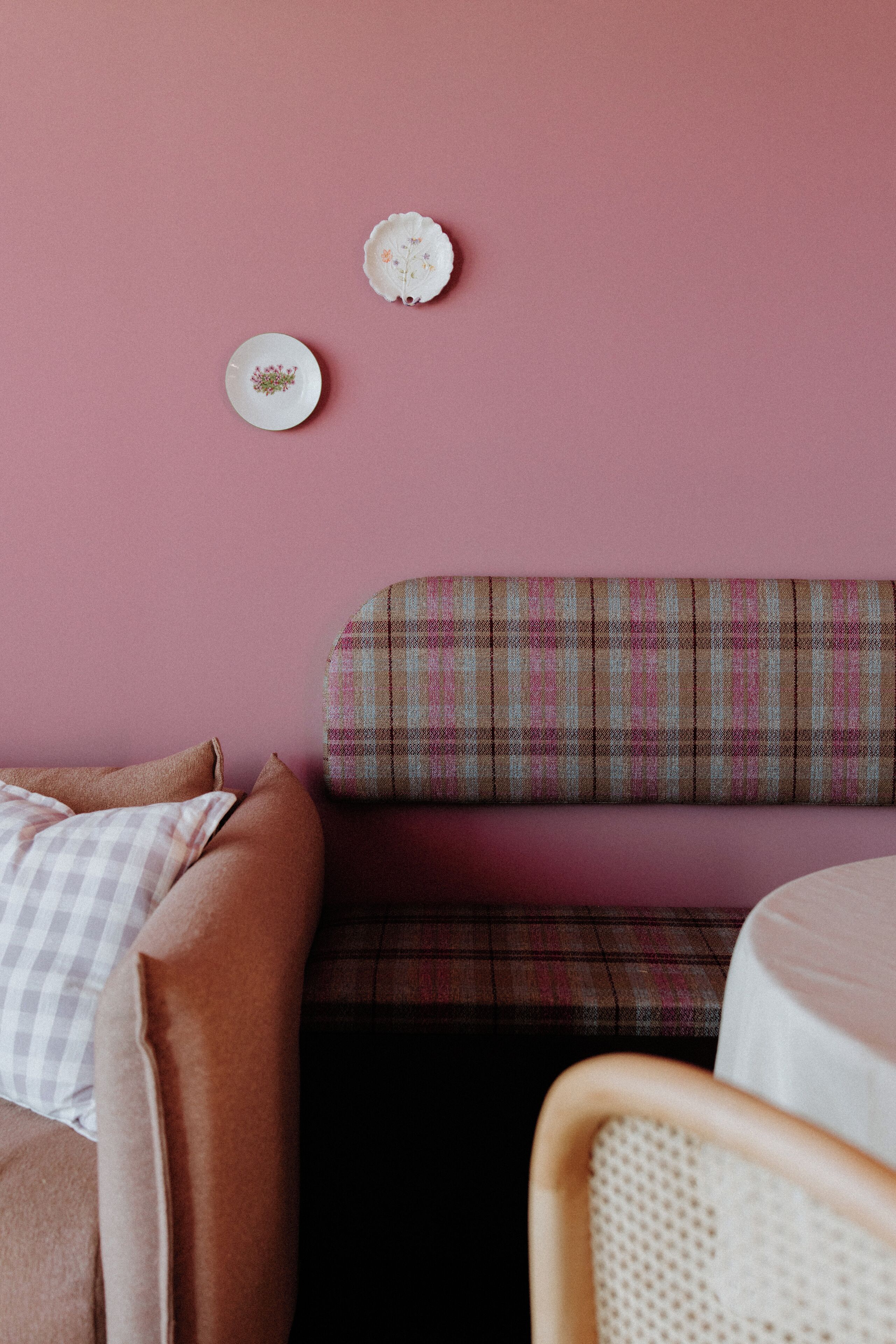 Una pared rosa con dos platos decorativos y un banco a cuadros.