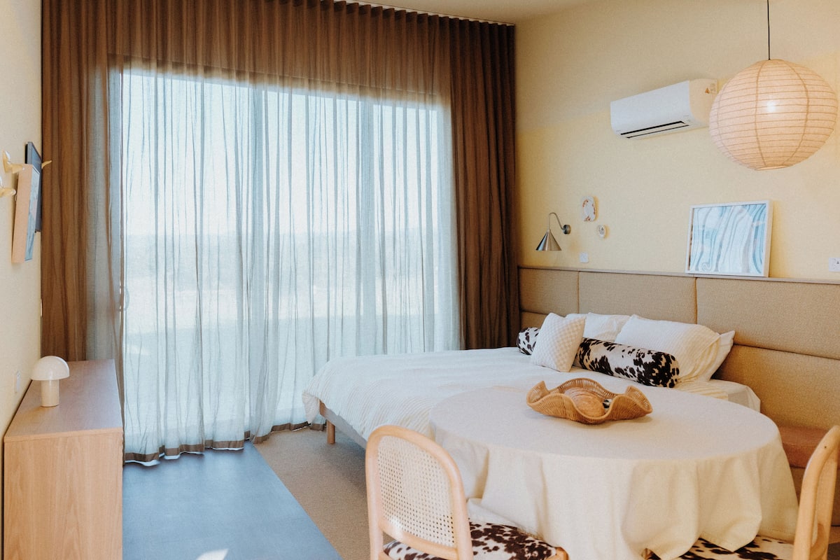 A hotel room with a large bed, a round table, a chair, a desk, and a window with curtains.