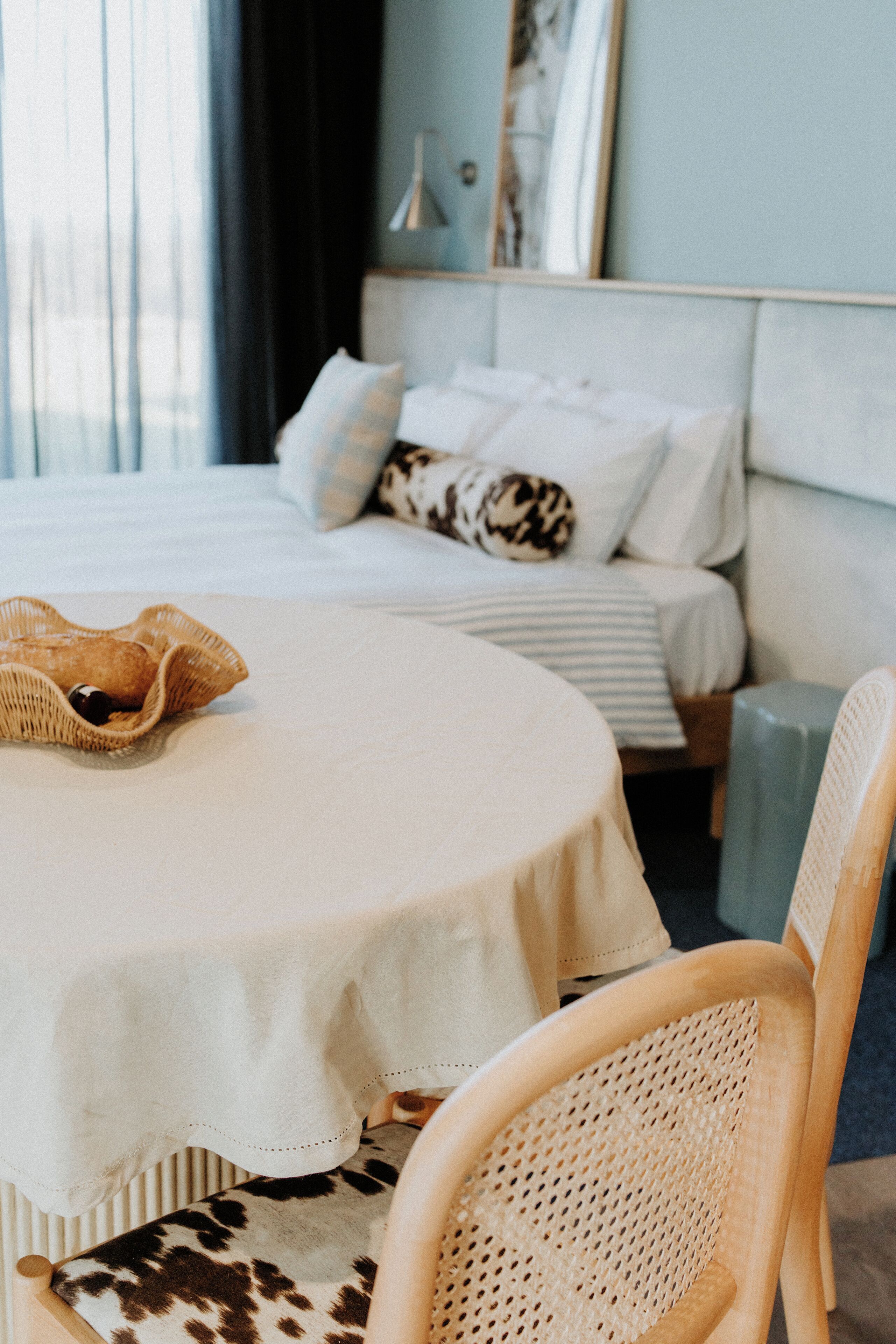 Une chambre bien rangée, avec un lit, une table de chevet, une chaise et une fenêtre avec des rideaux.