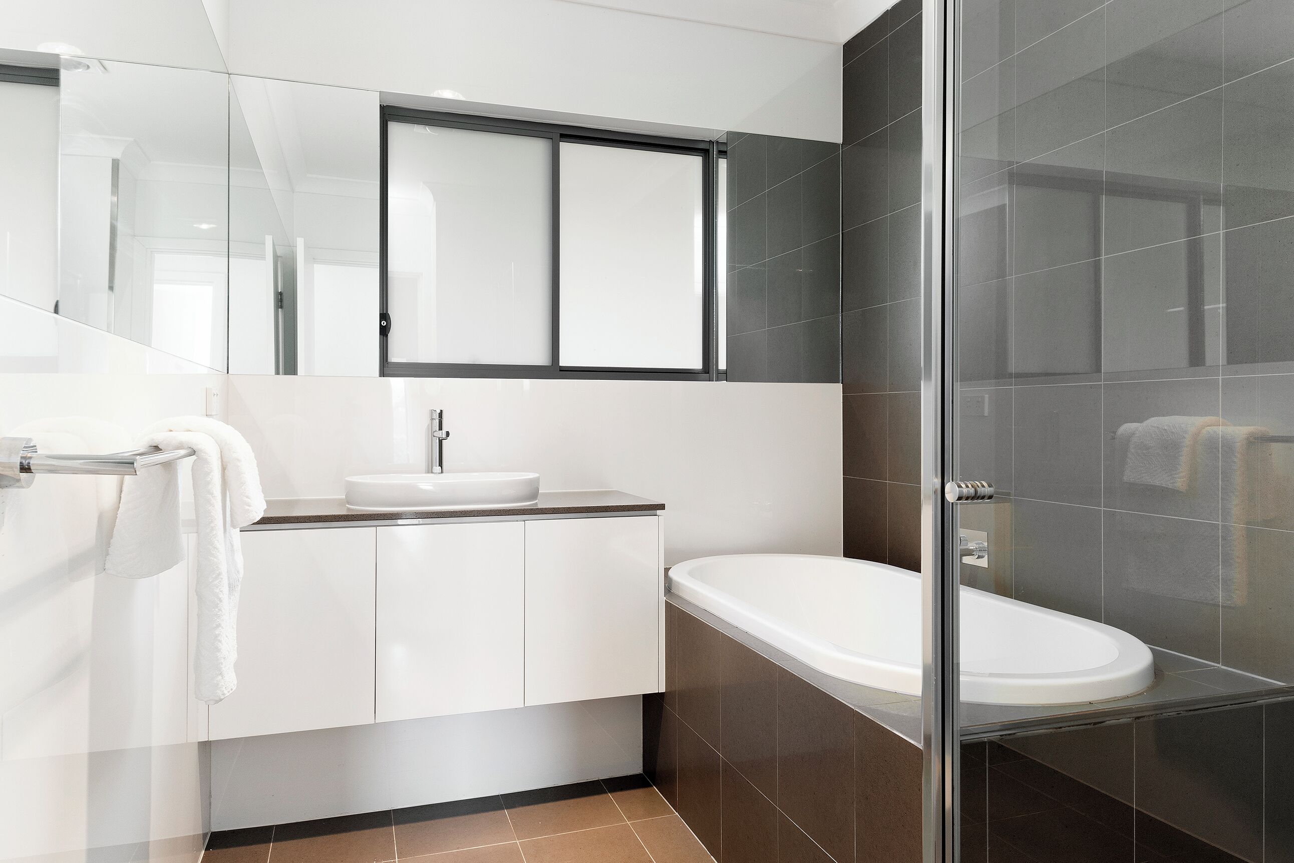 Un bagno moderno con cabina doccia in vetro, lavandino bianco e un ampio specchio sopra il mobile.