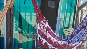 Une terrasse en bois avec une table bleue et un hamac rouge et blanc. On aperçoit au fond une porte sur laquelle est inscrit le nom « MARCOS ».