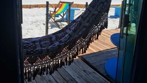 Un hamac sur une terrasse en bois, avec vue sur une plage et l’océan.