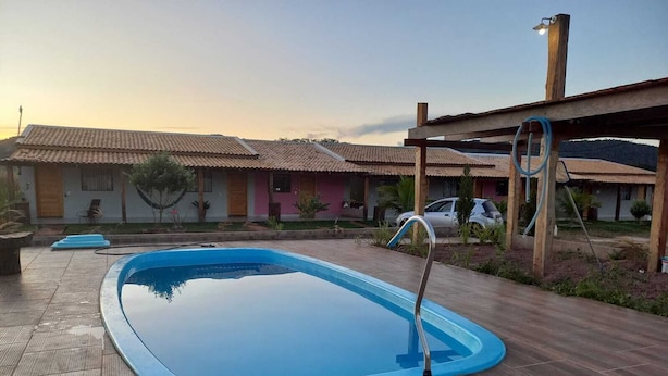 A swimming pool with a wooden deck, surrounded by houses with tiled roofs. - PORTAL DA LAGOA AZUL INN IN NOBRES (Coqueiral)