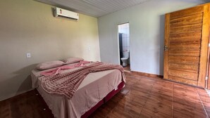 A bedroom with a bed, wooden flooring, a wooden door, and an air conditioning unit on the wall. - PORTAL DA LAGOA AZUL INN IN NOBRES (Coqueiral)