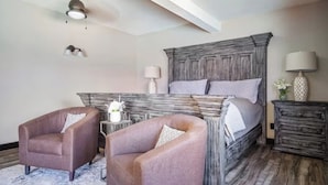 A bedroom with a large wooden bed, two armchairs, a nightstand, and a dresser.