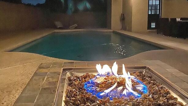 A swimming pool with a fire feature in the center, surrounded by stone tiles.