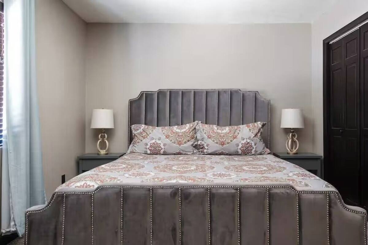 Un dormitorio con una cama grande, dos lámparas de noche, un armario oscuro y una ventana con persianas.