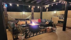 An outdoor patio area with a fire pit, seating, and potted plants.