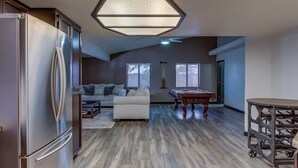 A modern kitchen with a stainless steel refrigerator, a dining table with a metal frame, and a pool table.