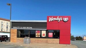 Ein Wendy's Restaurant mit roter und schwarzer Fassade, blauem Himmel und einem Parkplatz im Vordergrund.