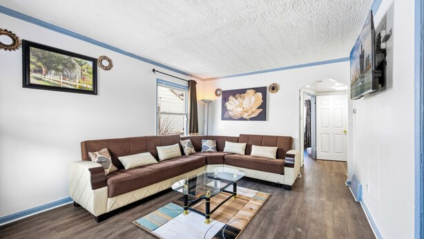 Een woonkamer met een hoekbank, een glazen salontafel en een kamerbreed tapijt met een patroon.