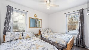 Een slaapkamer met twee bedden, een plafondventilator en een raam met gordijnen.