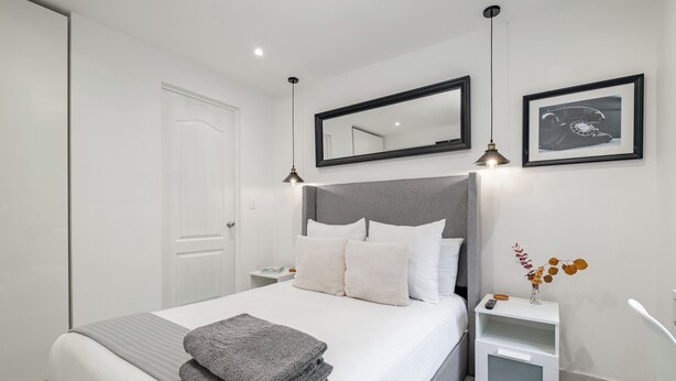 A modern bedroom with a large bed, bedside tables, a nightstand, a mirror, and framed pictures on the wall. - Casa AMA (Mexico City)