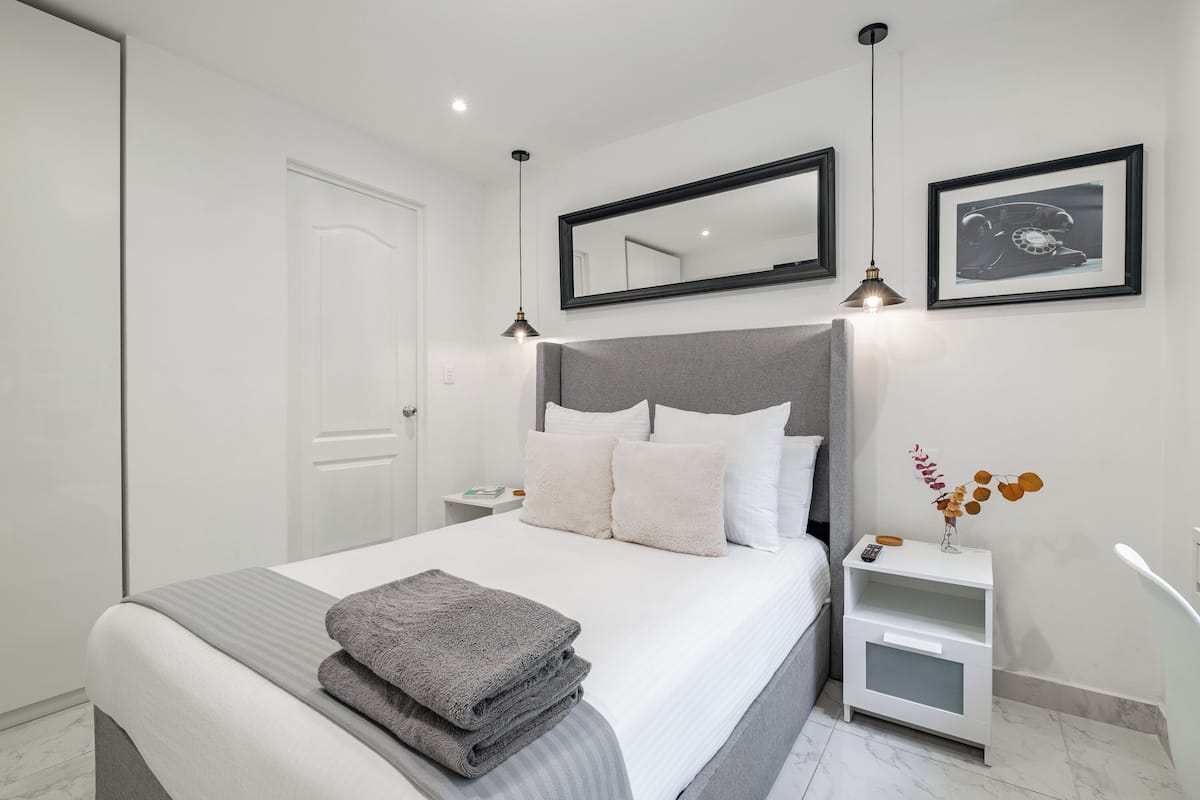 A modern bedroom with a large bed, bedside tables, a nightstand, a mirror, and framed pictures on the wall.
