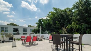 An outdoor patio area with a table and chairs, potted plants, and a view of a building and trees. - Casa AMA (Mexico City)