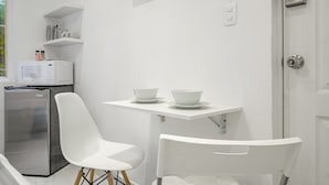 A modern kitchen with white cabinetry, a microwave, a refrigerator, and two white chairs at a small table. - Casa AMA (Mexico City)