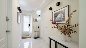 A hallway with a white door, a framed picture on the wall, and a vase with dried flowers on a console table. - Casa AMA (Mexico City)