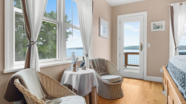 Ein Zimmer mit Korbmöbeln, einem Bett, einem Tisch mit weißem Tuch und einer Tür, die auf einen Balkon führt.