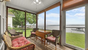 Eine überdachte Veranda mit Korbmöbeln, einem Holztisch und Blick auf ein Gewässer.