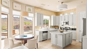 Een moderne keuken met grijze kastjes, een centraal eiland en een eethoek met een ronde tafel en stoelen.