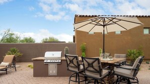 An outdoor patio with a grill, dining table, chairs, and a large umbrella. - 4BR The Talon Trail Home: Pool, Spa,  Golf Access (Scottsdale)