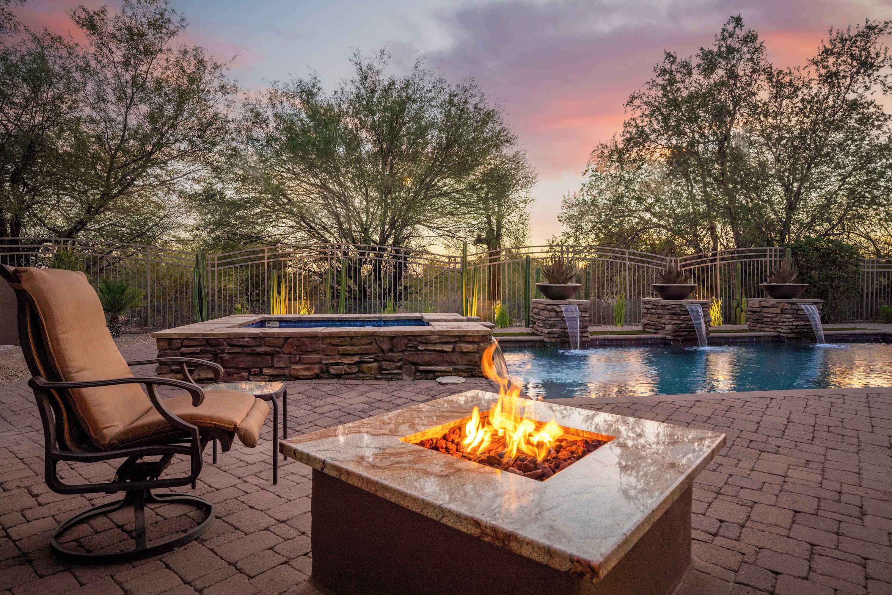 A fire pit with a pool and waterfall feature in a landscaped outdoor area.