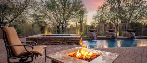 A fire pit with a pool and waterfall feature in a landscaped outdoor area.