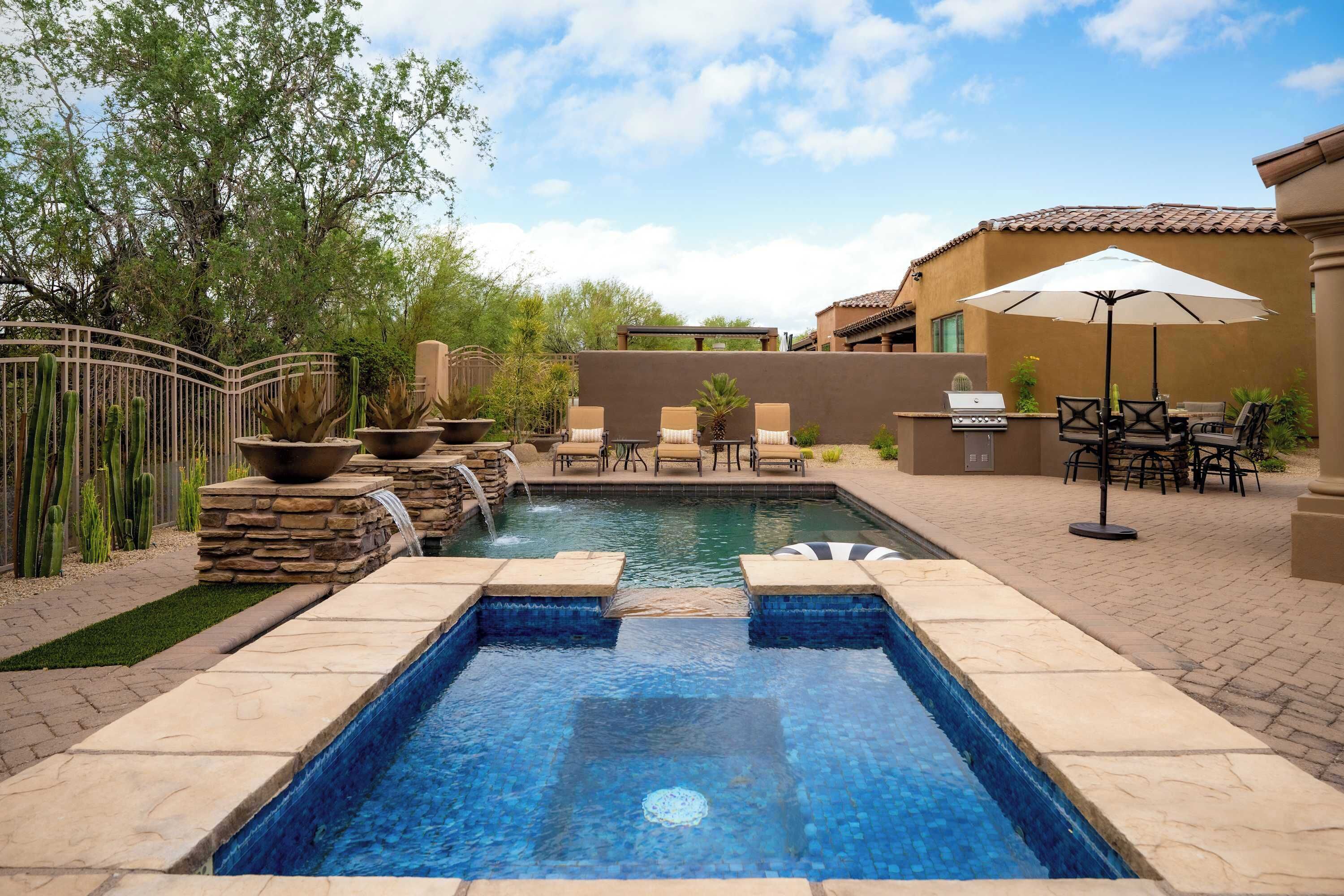 A swimming pool with a hot tub, surrounded by patio furniture and a cactus garden.