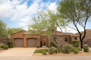 Una propiedad residencial con fachada de estuco marrón, techo de tejas y un jardín delantero bien cuidado con cactus y arbustos.