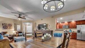 A spacious living room with a large wooden dining table, a ceiling fan, and a modern kitchen with wooden cabinets and stainless steel appliances. - Beautiful pool oasis near TPC Scottsdale (Scottsdale)