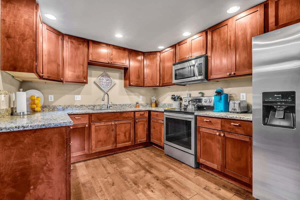 A kitchen with wooden cabinets, a stainless steel refrigerator, a microwave, an oven, and granite countertops.