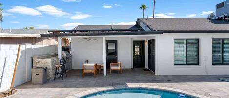 A residential backyard with a swimming pool, a barbecue area, and a covered patio with seating.
