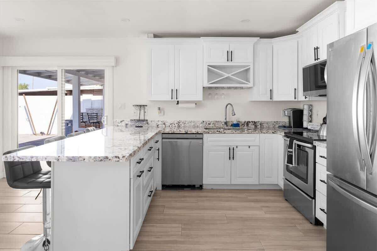 A modern kitchen with white cabinets, a stainless steel refrigerator, and a granite countertop.