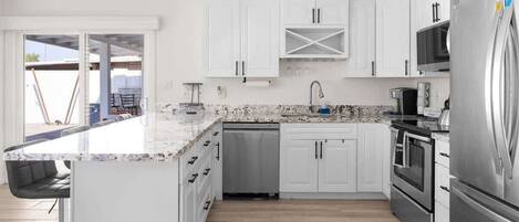 A modern kitchen with white cabinets, a stainless steel refrigerator, and a granite countertop.