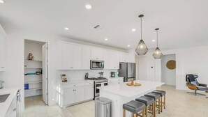 Una cocina moderna con armarios blancos, una isla grande con taburetes, electrodomésticos de acero inoxidable e iluminación colgante.