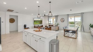 Cocina moderna con armarios blancos, una isla central e iluminación colgante.