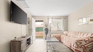A living room with a sofa, a coffee table, a TV mounted on the wall, and a door leading outside. - Exclusive BBQ oasis, mins to Papago Park (Phoenix)