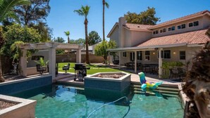 Una piscina con un jacuzzi, rodeada por una terraza con mobiliario exterior y palmeras.